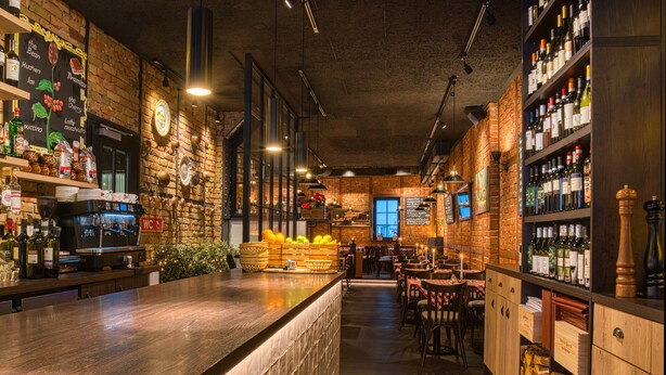 A bar with a wooden counter, shelves with bottles, and a brick wall. - UNO Hotel Hamburg Central 053 (Hamburg)