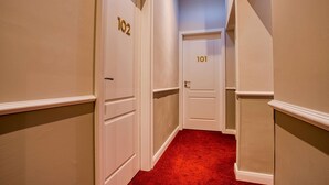 A hallway with doors numbered 101 and 102, carpeted in red, and white walls with trim. - UNO Hotel Hamburg Central 053 (Hamburg)