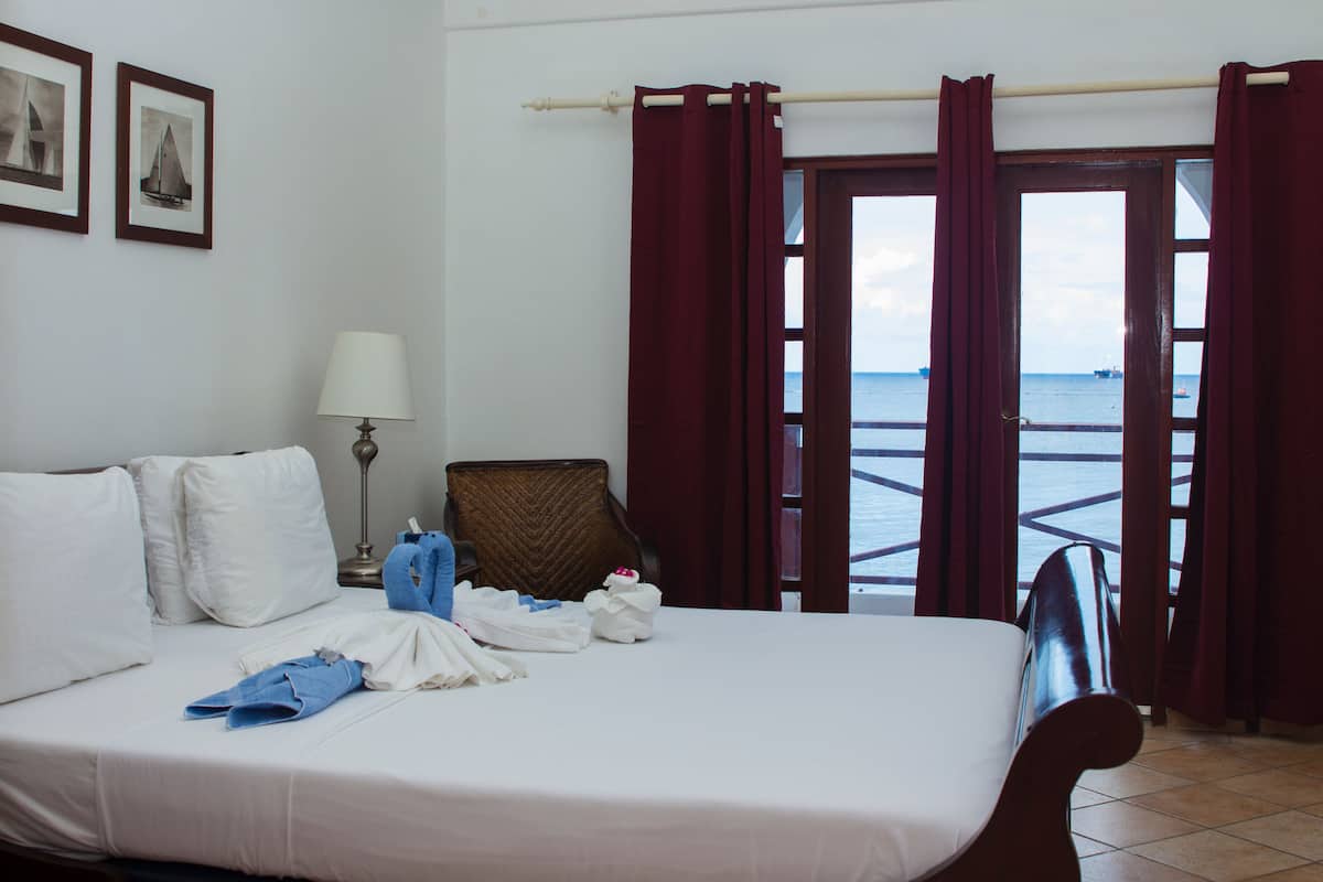 A hotel room with a bed, a chair, a lamp, and a view of the sea through a door.