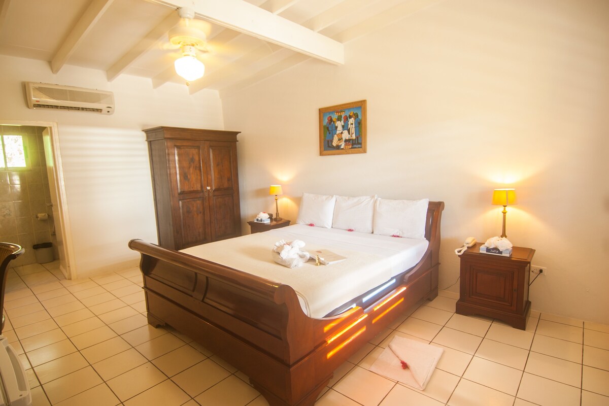 Un dormitorio con una cama de madera, dos lámparas de noche, una mesita de noche, un armario de madera y un aire acondicionado instalado en la pared.