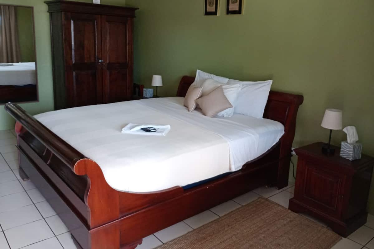 A neatly made bed with a white comforter and pillows, a wooden headboard, a nightstand with a lamp, and a wall-mounted air conditioner.