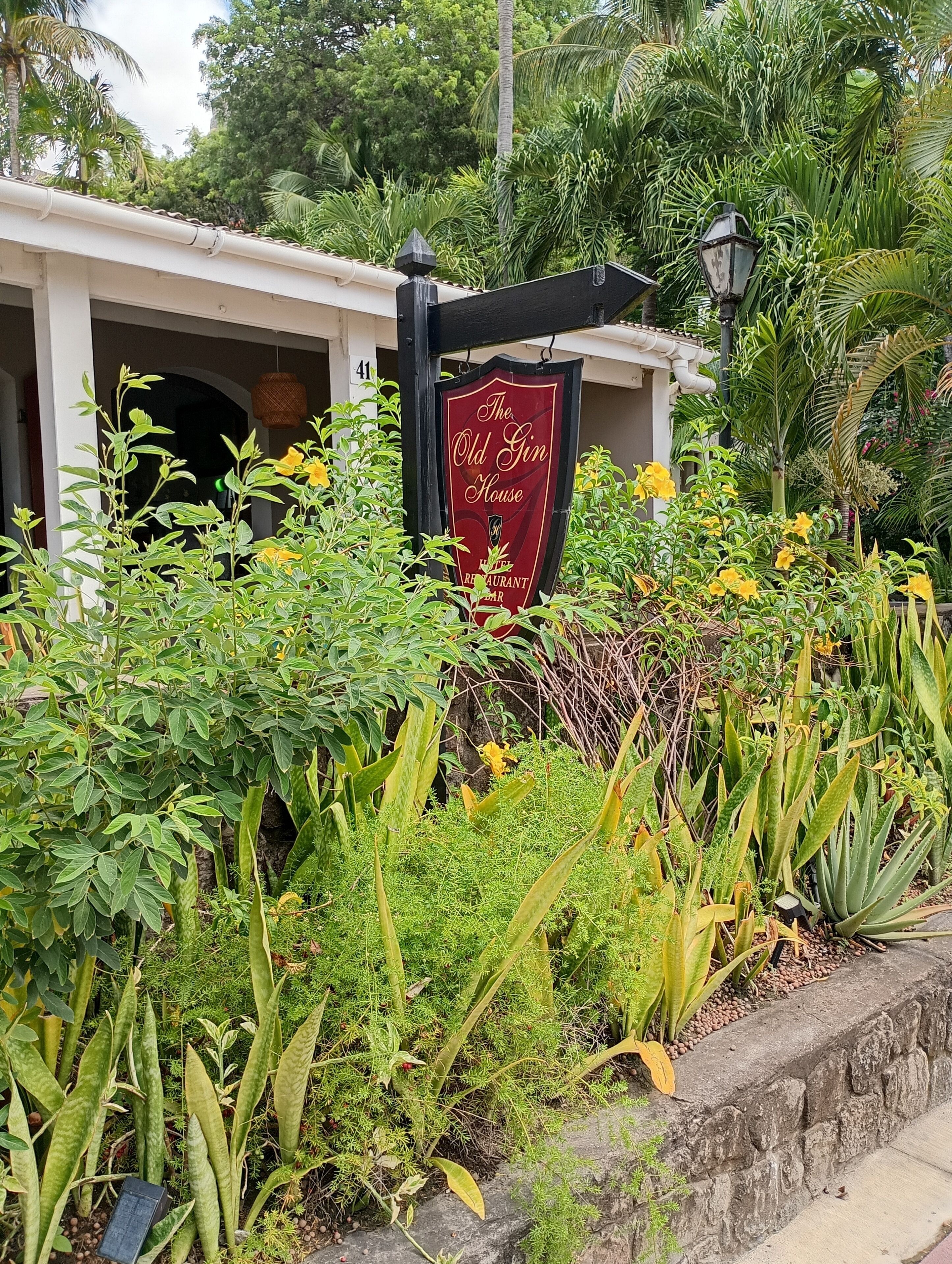 A sign for "The Old Gin House" restaurant surrounded by lush greenery and tropical plants.