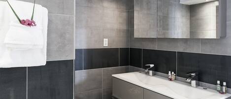 A modern bathroom with two sinks, a large mirror, and grey tiles.