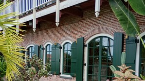 Een bakstenen gebouw met een balkon, groene luiken en een tuin met verschillende planten.