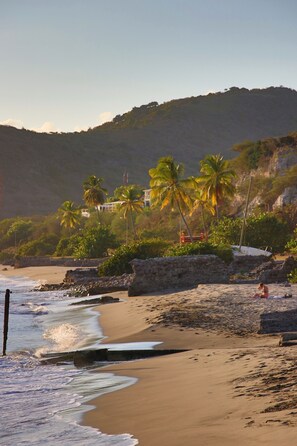 A beach with palm trees, a stone wall, and a building in the background.