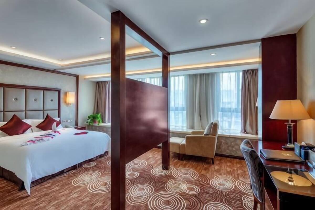 Une chambre d’hôtel avec un grand lit, un bureau, une chaise et une fenêtre avec des rideaux.