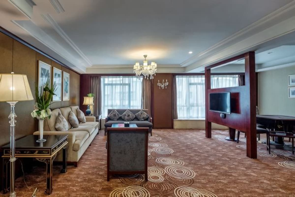 A hotel room with a sofa, armchair, TV, and a patterned carpet.