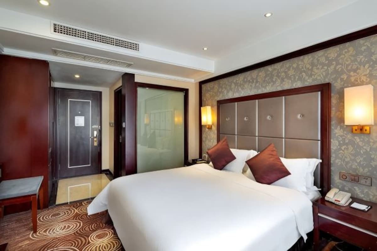 A hotel room with a large bed, bedside table, lamp, and a door leading to another room.