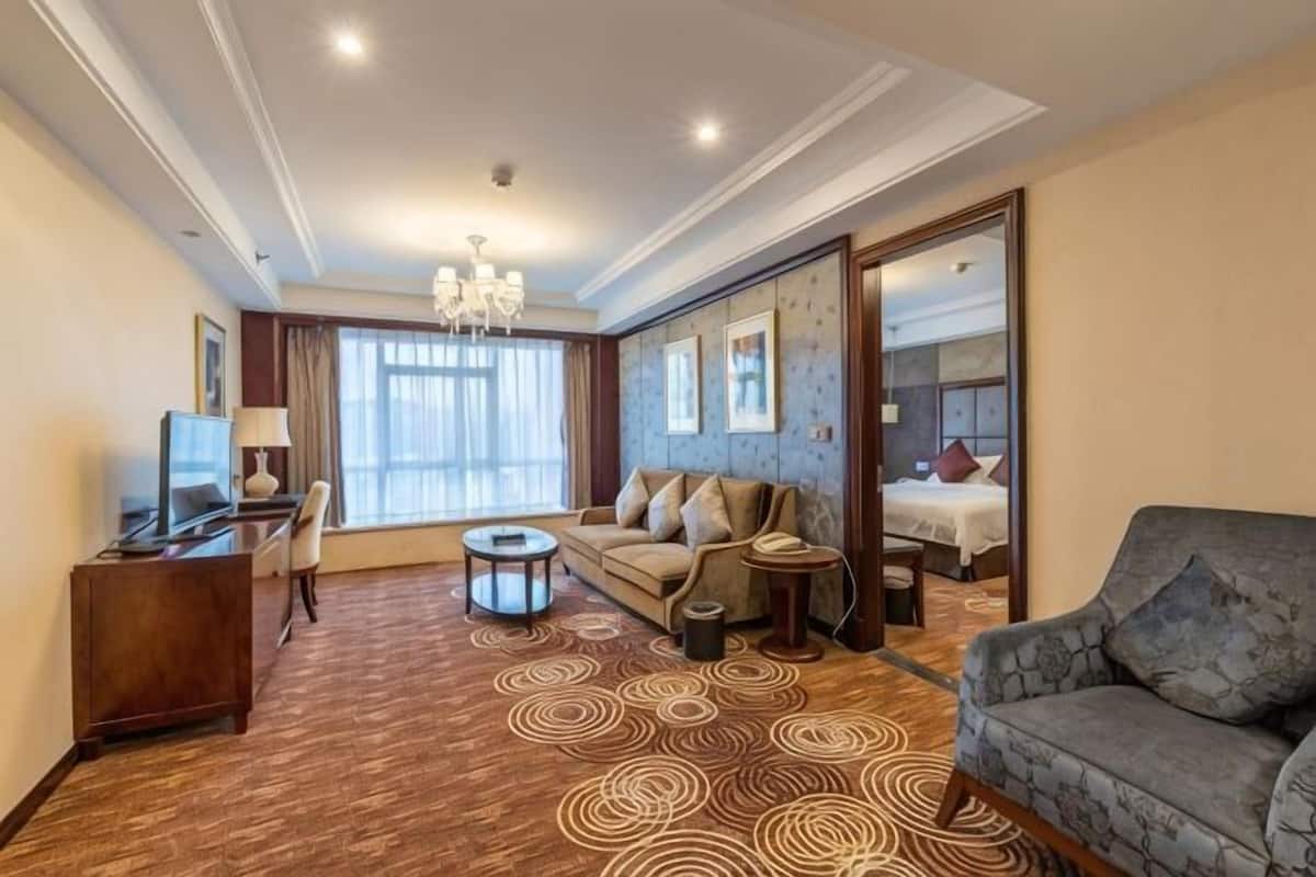 Une chambre d’hôtel avec un canapé, un fauteuil, une table basse, une télévision et un lit.