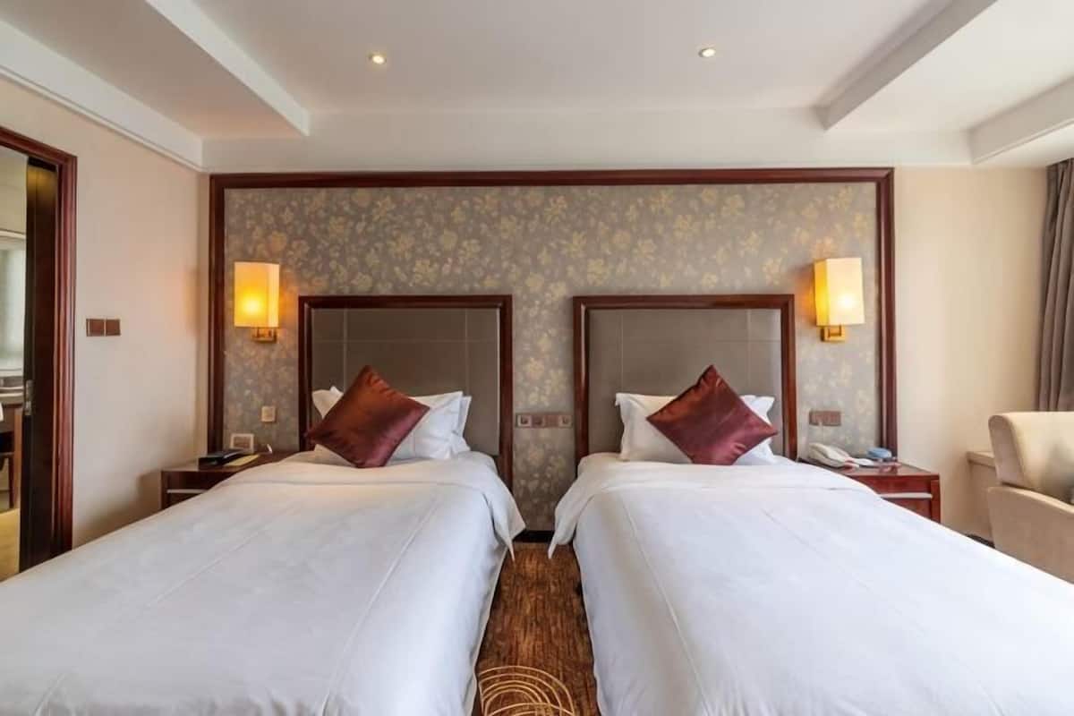 Une chambre d’hôtel avec deux lits, une table de chevet, une chaise et une lampe fixée au mur.