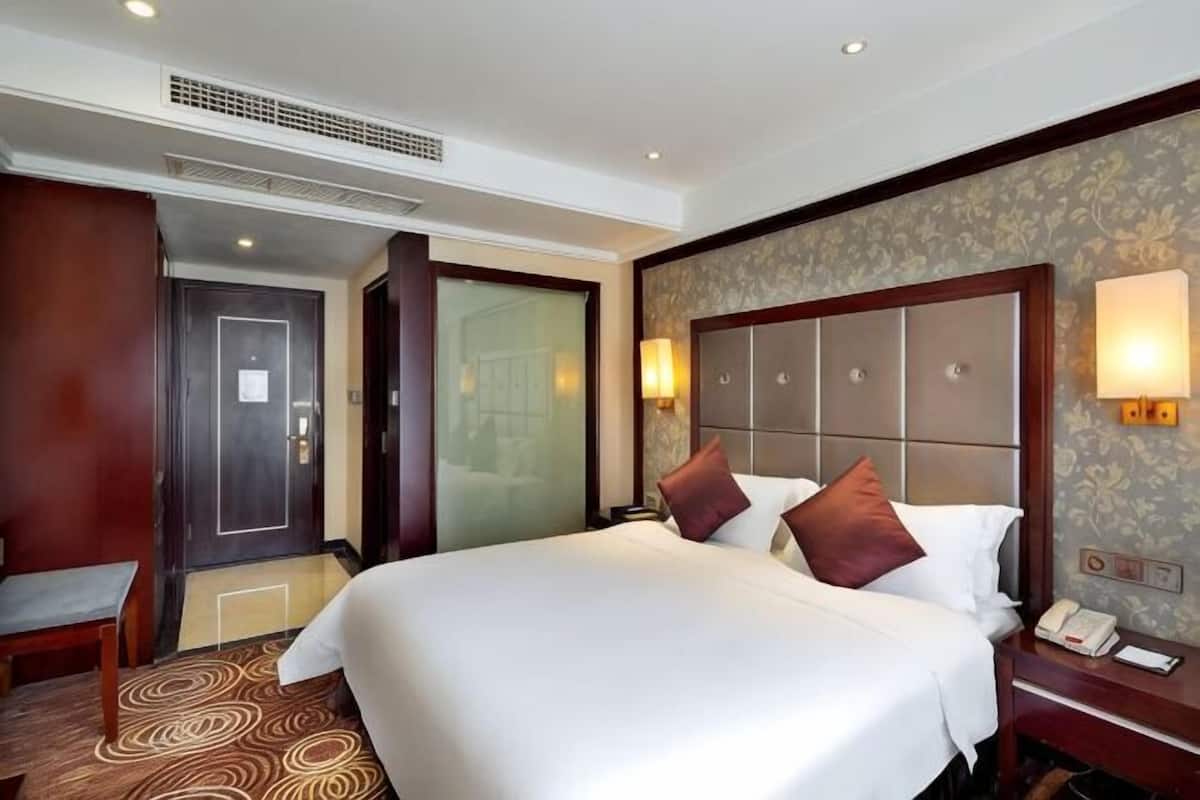 Une chambre d’hôtel avec un grand lit, une table de chevet, une commode, un bureau et une chaise.