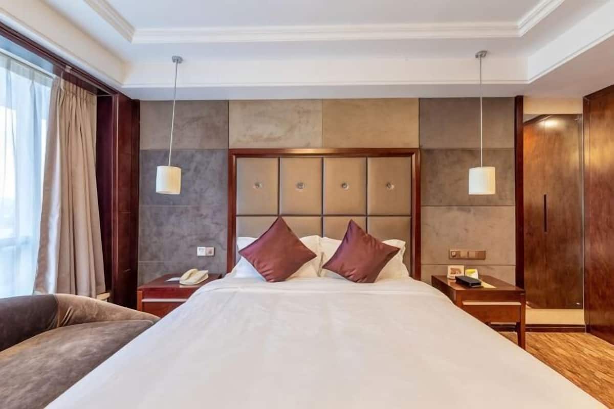 Une chambre d’hôtel avec un grand lit, une table de chevet avec une lampe, un téléphone et une armoire en bois.