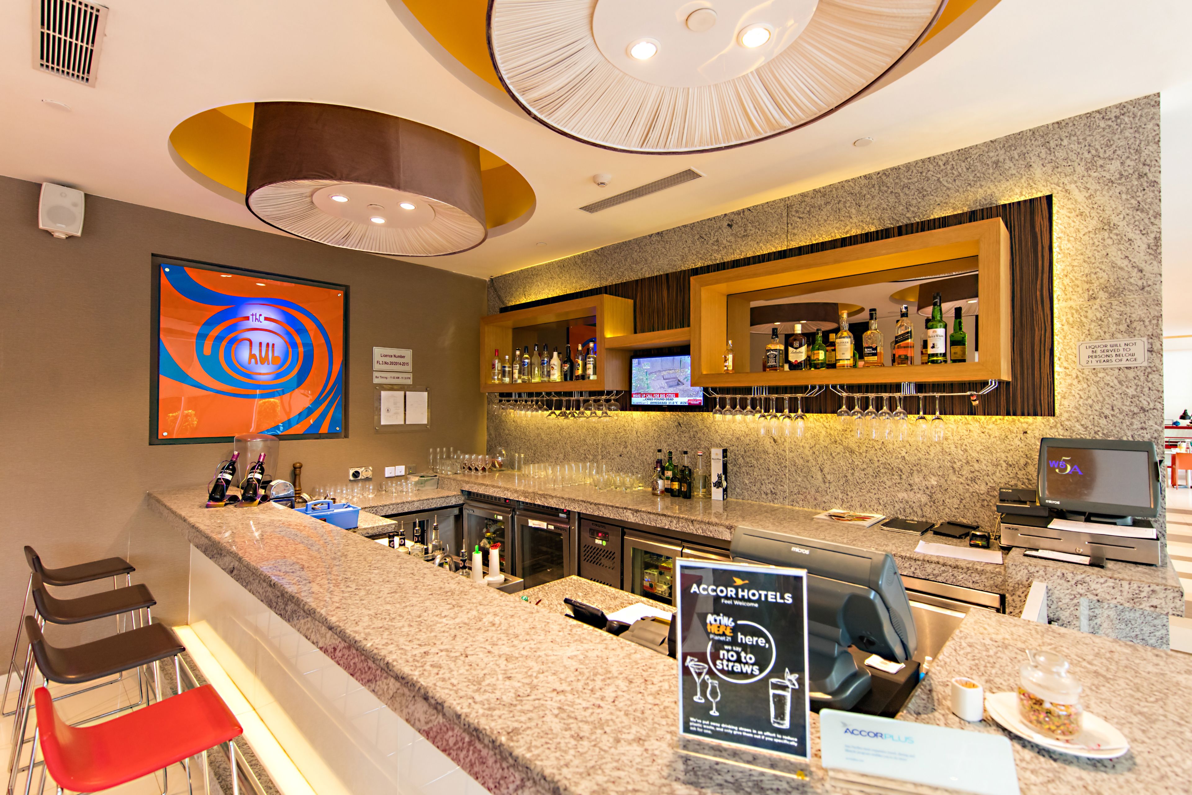 Bar de hotel com bancada de granito, banquetas, uma televisão e um aviso indicando que canudos não são permitidos.