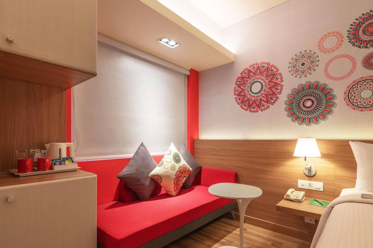 A modern hotel room with a red sofa, a small white table, and a lamp.