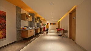 A modern hotel corridor with a kitchen area on the left, a seating area with a red chair, and a wooden door on the right. - ibis Chennai SIPCOT Hotel (Tirupporur)