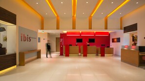 A modern hotel lobby with a reception desk, a bench, and a wall with the hotel's name. - ibis Chennai SIPCOT Hotel (Tirupporur)