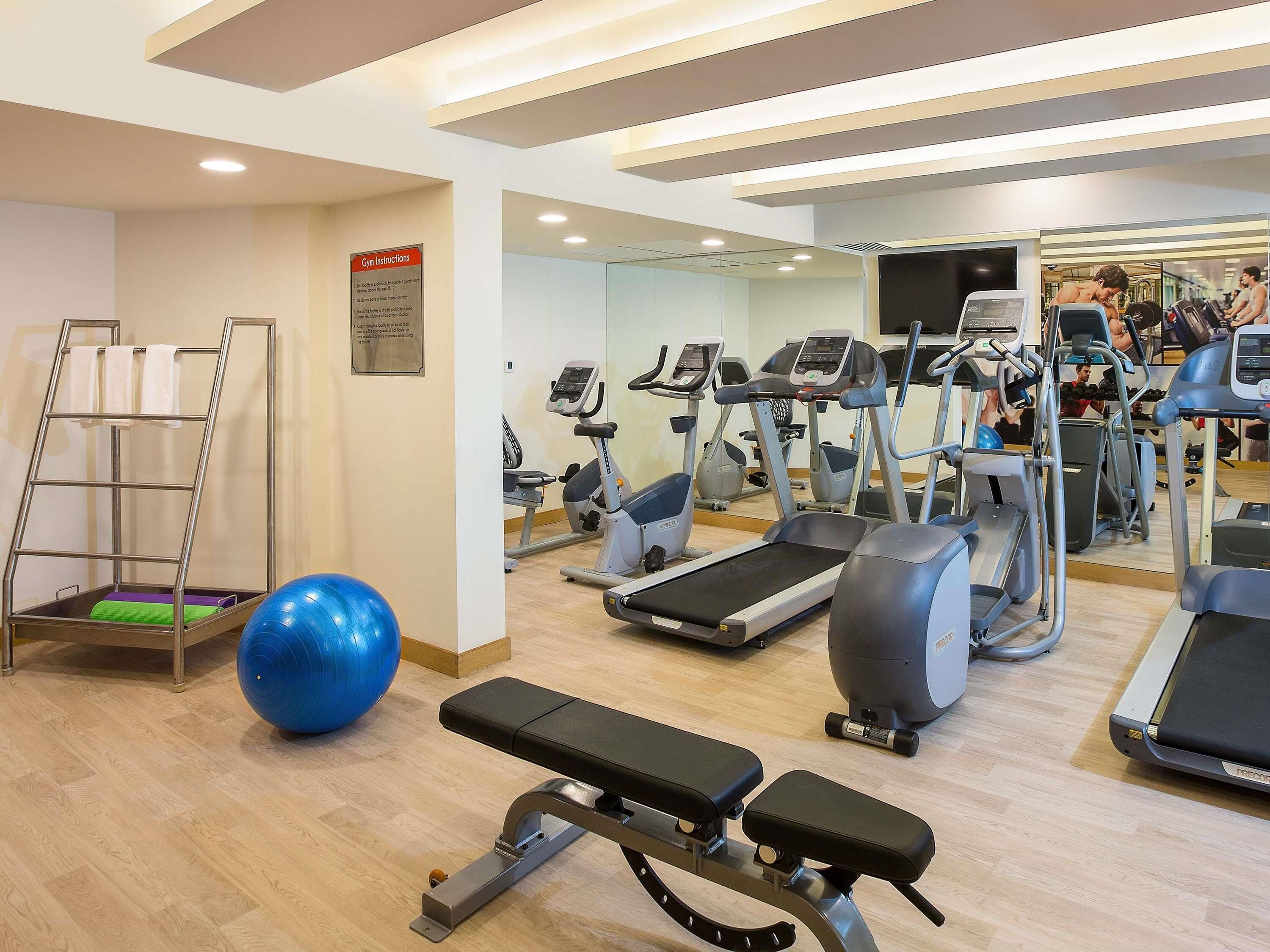 Ein Fitnessraum mit Laufbändern, Crosstrainern, einer Bank, einem blauen Übungsball und einer Leiter.