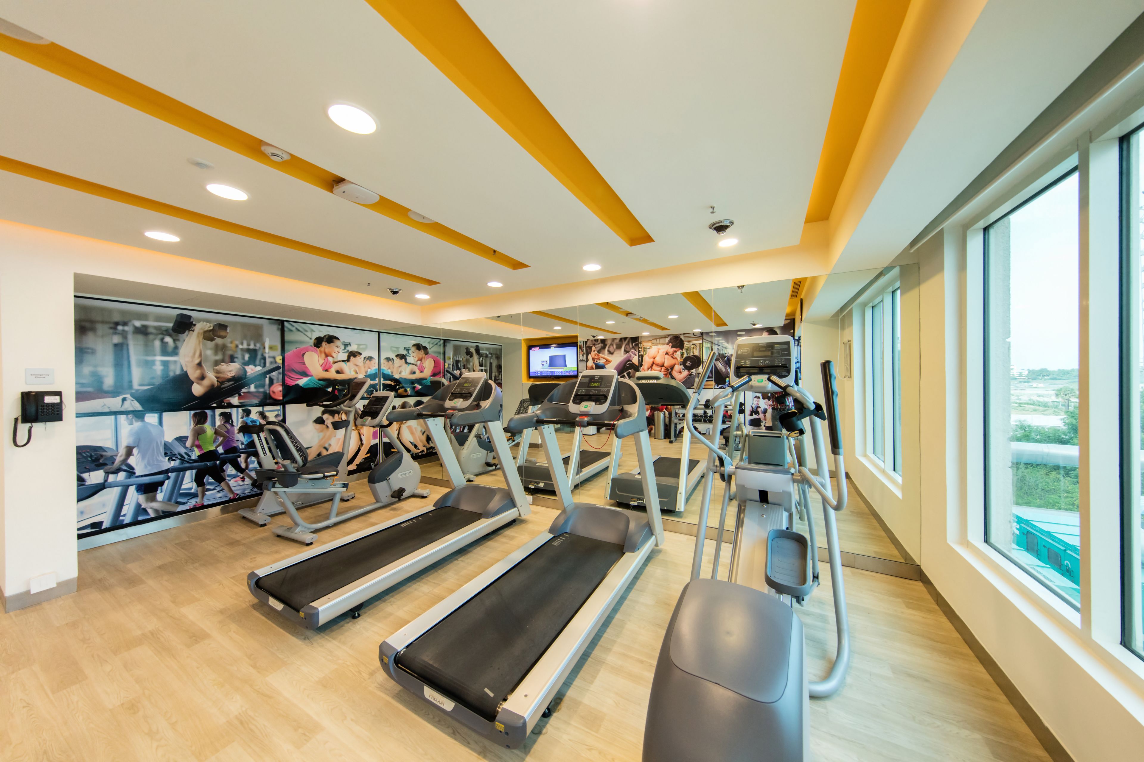 A gym with treadmills, exercise bikes, and a television screen.