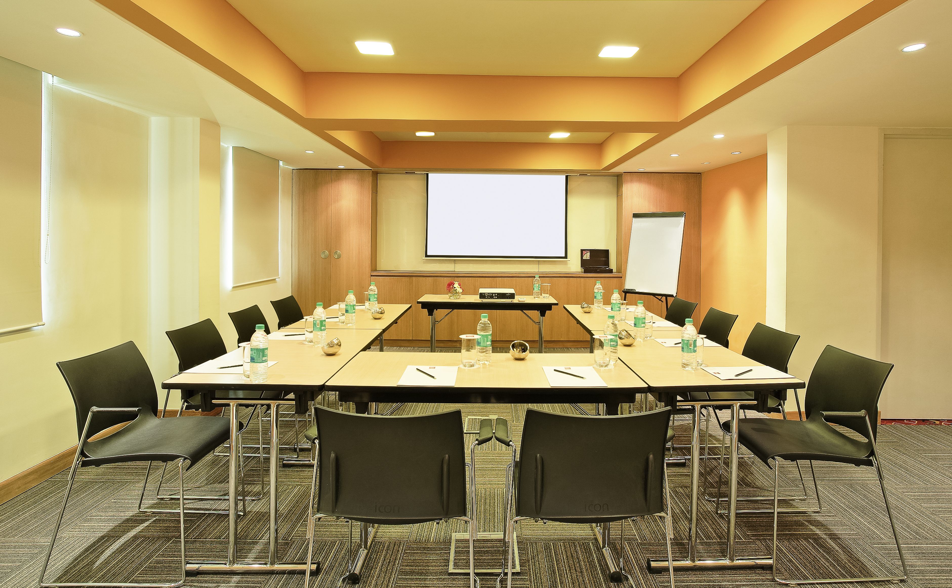 A conference room with a long table, chairs, a projector screen, and a whiteboard.