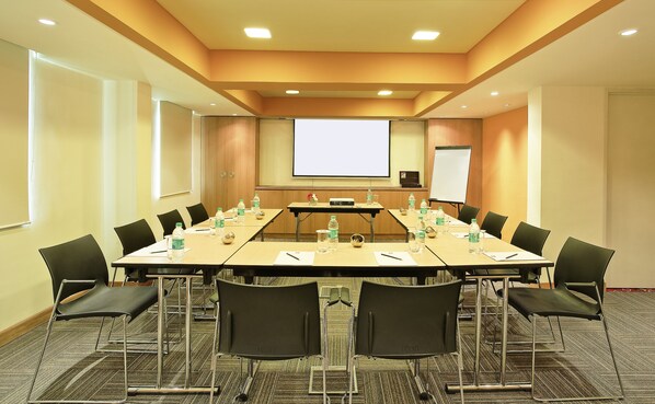 Una sala de conferencias con una mesa larga, sillas, una pantalla de proyector y una pizarra.