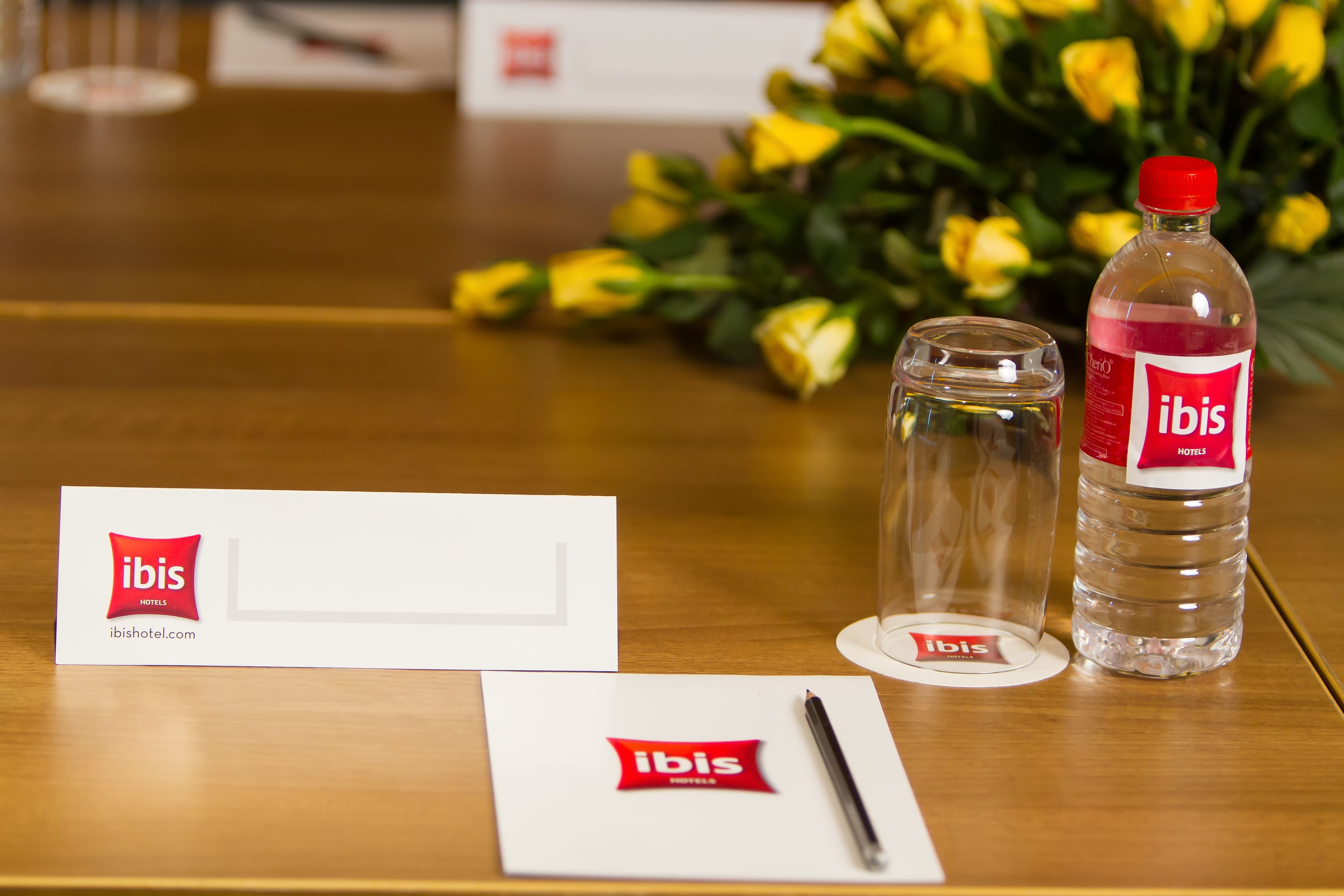 Un comptoir d’accueil d’hôtel avec un présentoir à cartes de visite, un stylo, un verre et une bouteille d’eau.