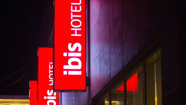 A building with large glass windows and red signage indicating it is the ibis hotel. - ibis Chennai SIPCOT Hotel (Tirupporur)