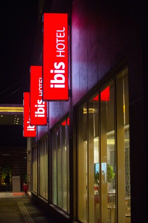 A building with large glass windows and red signage indicating it is the ibis hotel. - ibis Chennai SIPCOT Hotel (Tirupporur)