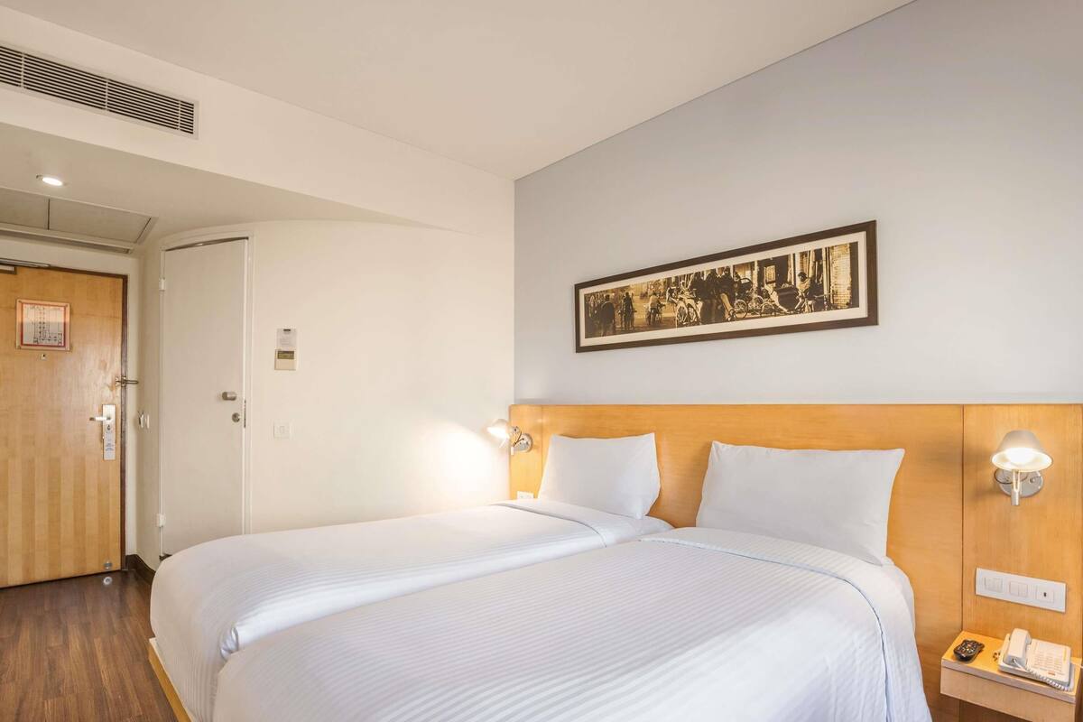 Un cuarto de hotel con una cama grande, un cabecero de madera, una mesita de noche con teléfono y un cuadro enmarcado en la pared.