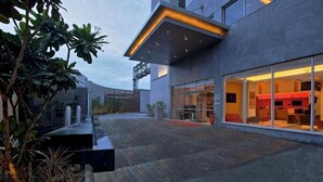 A modern building with a glass facade, a courtyard with a water feature, and a red interior visible through the windows. - ibis Chennai SIPCOT Hotel (Tirupporur)