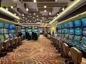 Ein Casino mit mehreren Spieltischen und Spielautomaten, angeordnet in Reihen auf einem gemusterten Teppich.