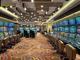 A casino with multiple gaming tables and slot machines, arranged in rows with a patterned carpet.