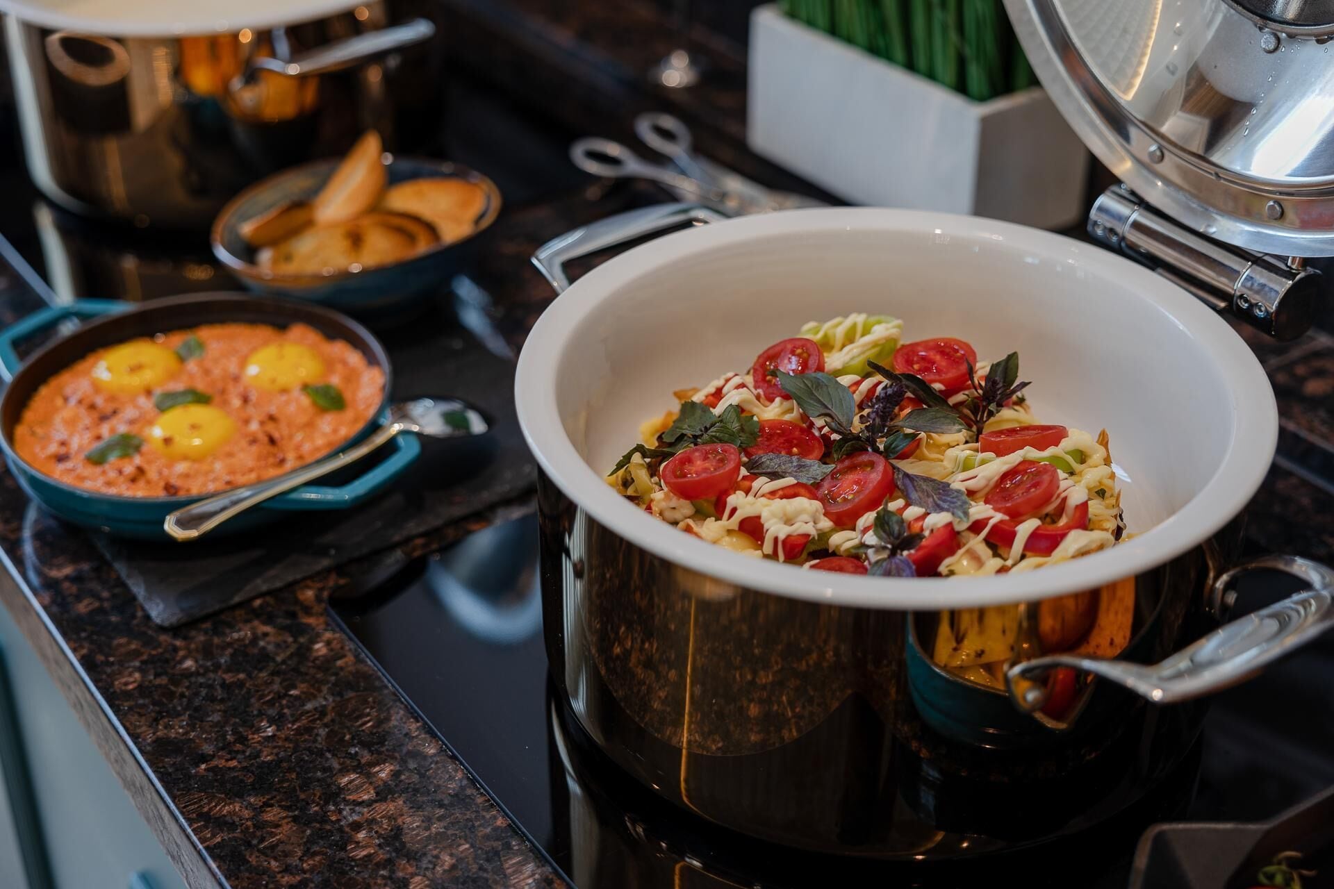 A kitchen with a stove, pots, and a bowl of pasta salad.