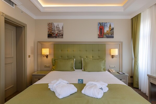 A hotel room with a large bed, two pillows, a bedside table with a lamp, a nightstand with a phone, and artwork depicting London landmarks. - Hotel London 1889 & Casino (Batumi)