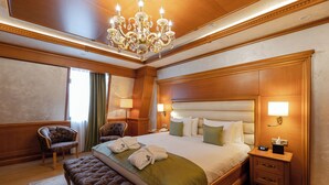 A spacious hotel room with a large bed, a bench, two armchairs, a chandelier, and a nightstand with a lamp. - Hotel London 1889 & Casino (Batumi)