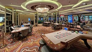 A casino with multiple gaming tables, a large chandelier, and a carpeted floor.