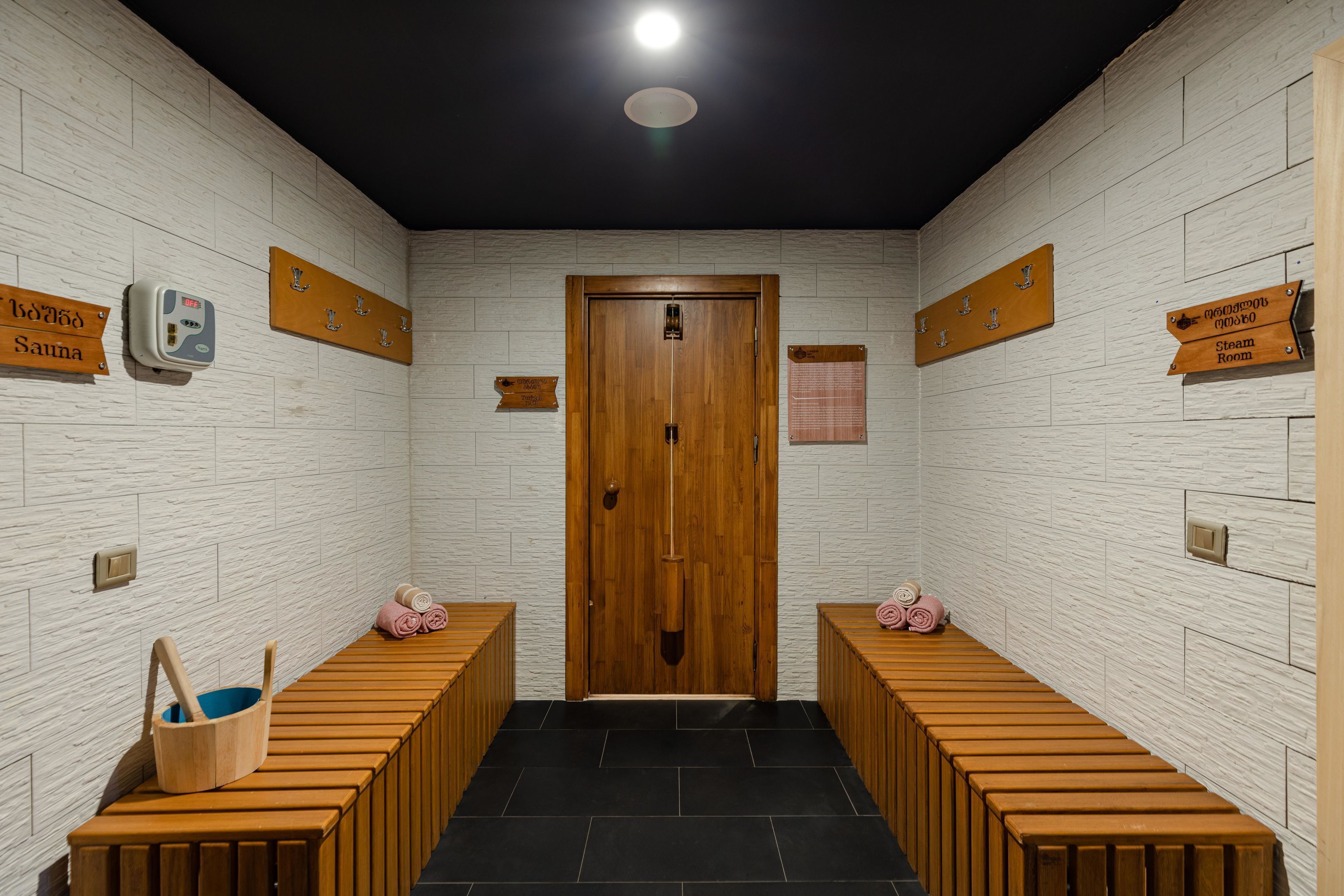 Un cuarto de spa con bancos de madera, una puerta de madera y señales que indican servicios como sauna y baño de vapor.