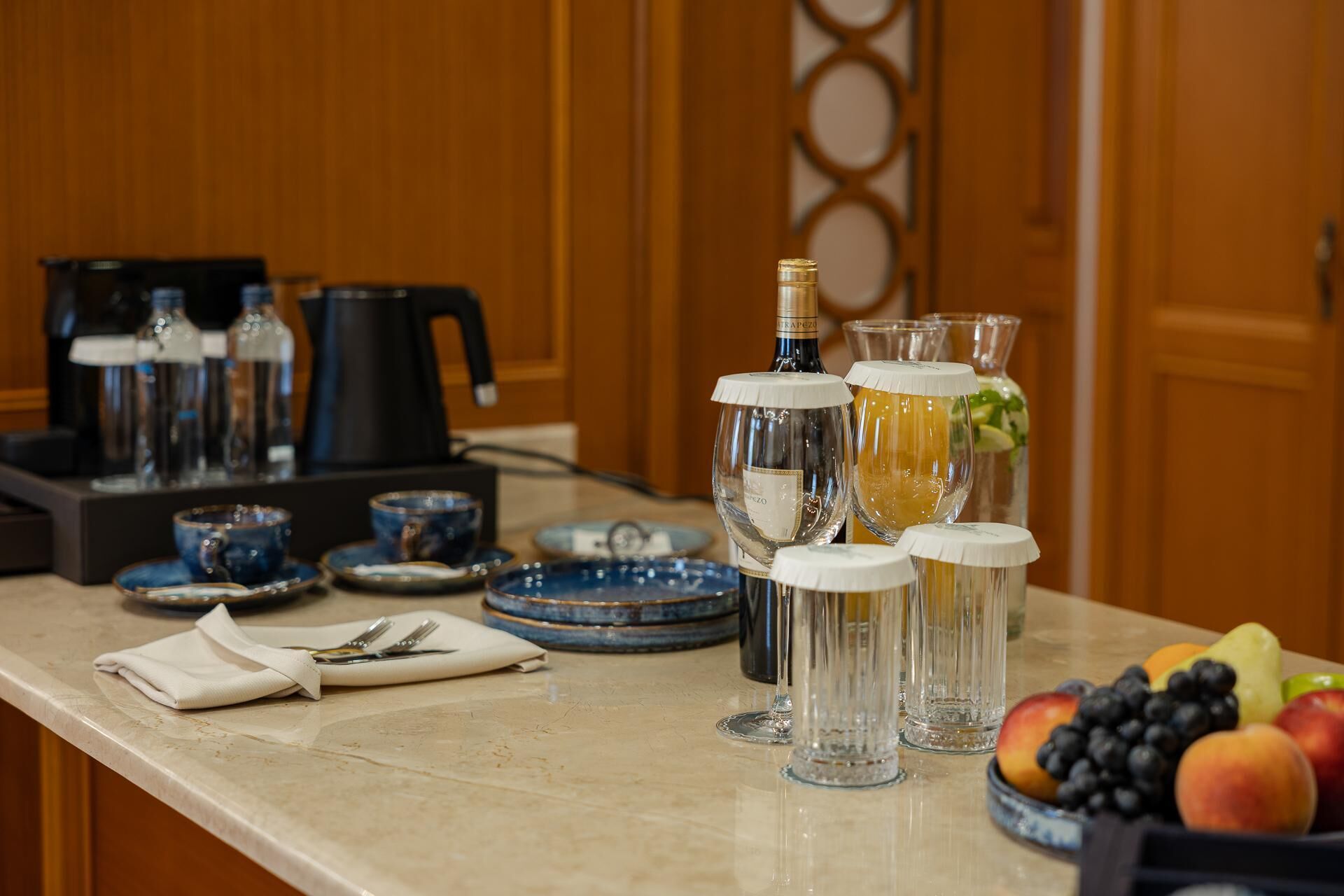 A kitchen counter with a coffee maker, wine bottles, glasses, and a fruit bowl.