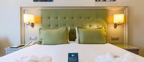 A hotel room with a large bed, two green pillows, two bedside lamps, and a nightstand with a phone and a lamp.