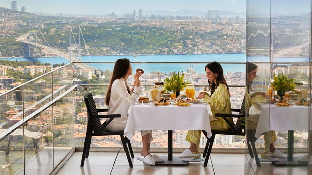 Un comedor con una mesa lista para cuatro, con vistas a un paisaje urbano y una masa de agua.