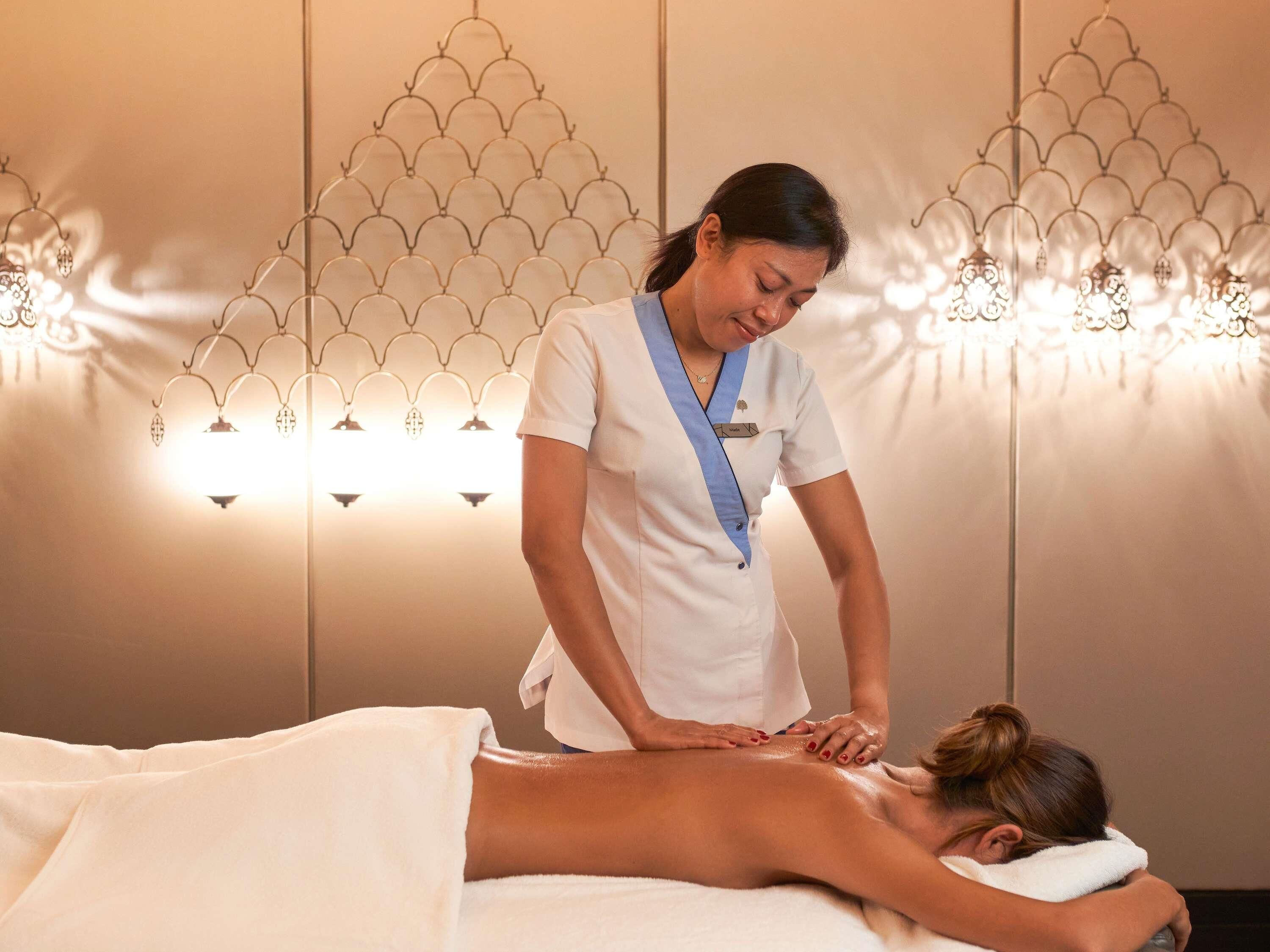 A massage therapy session in a room with a patterned wall and wall-mounted lights.