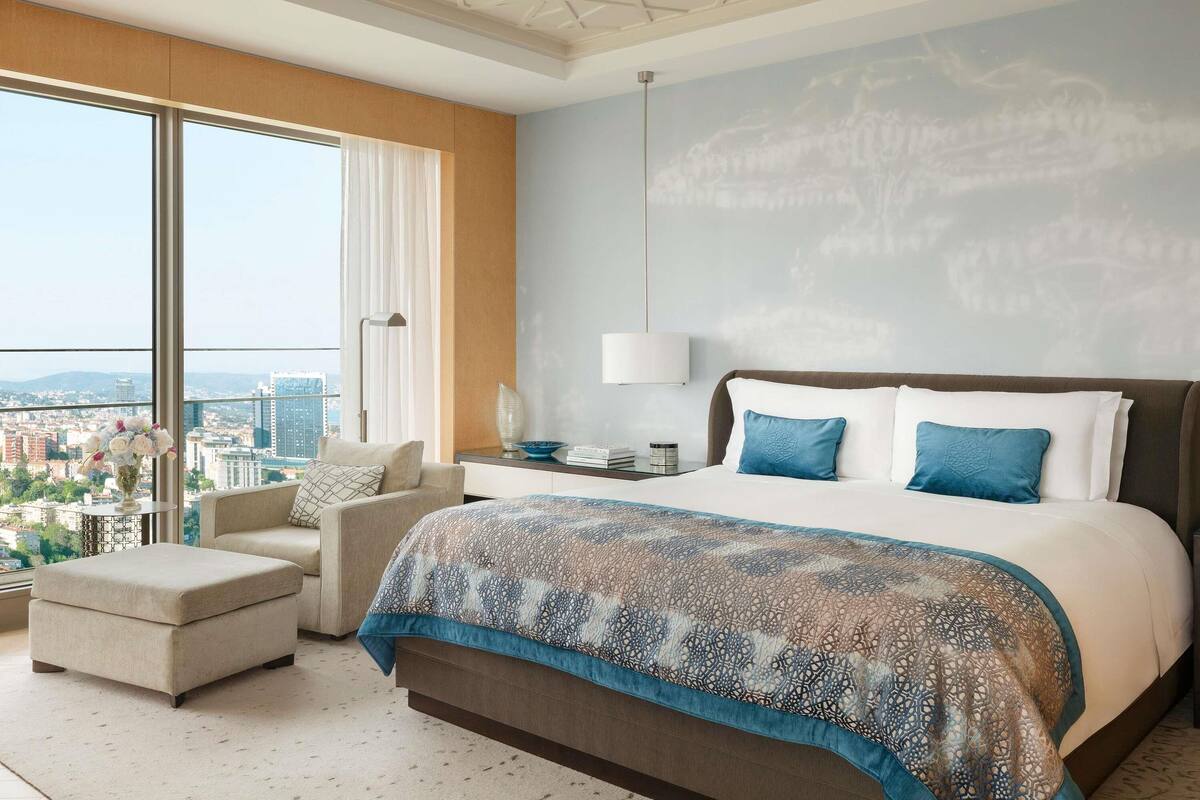A modern hotel room with a large bed, a sofa, a small table, and a view of the city.