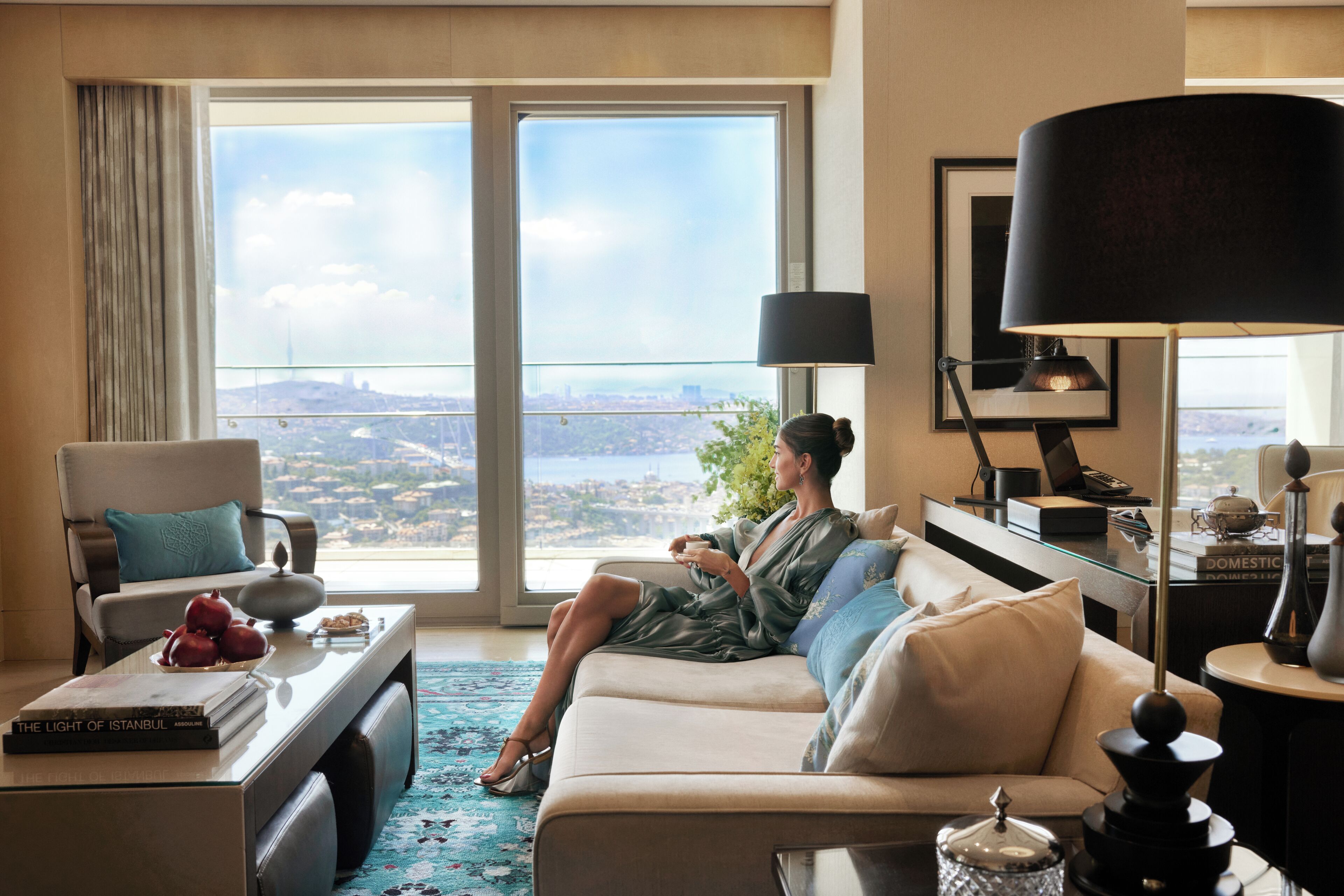 A room with a large window, a sofa, a coffee table, and a desk with a lamp.