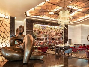 A modern lobby with a large abstract sculpture, a grand chandelier, and a large mural of a historic building.