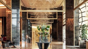 Un vestíbulo espacioso con suelo de mármol pulido, una gran lámpara decorativa y un arreglo floral central.
