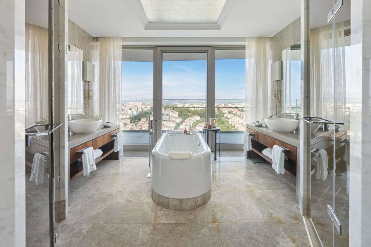 A modern bathroom with a large bathtub, two sinks, and a city view.