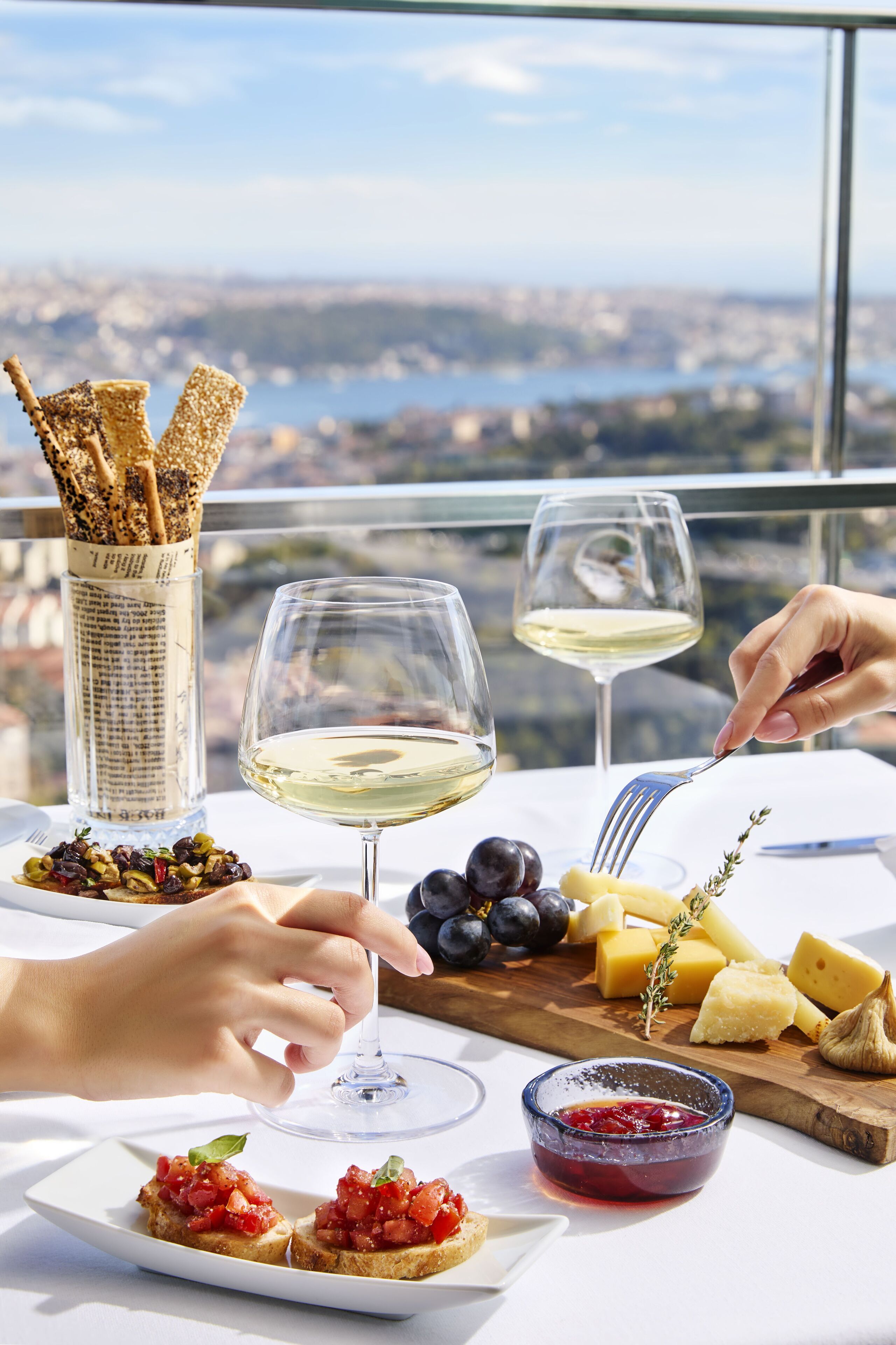 A table set with cheese, grapes, crackers, and a bowl of jam, with a scenic view in the background.