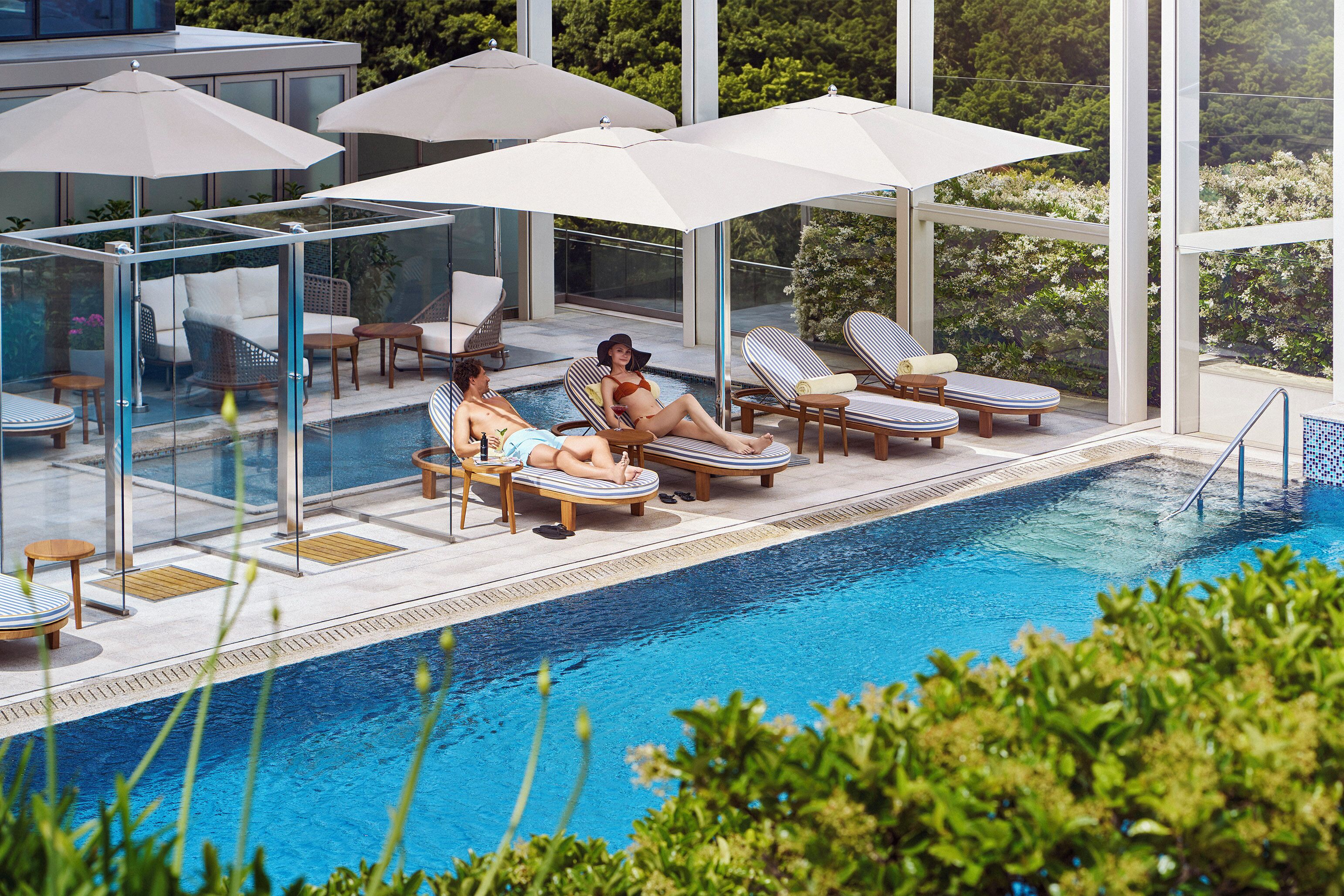 A poolside area with lounge chairs, umbrellas, and a glass-enclosed seating area.