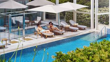 A poolside area with lounge chairs, umbrellas, and a glass-enclosed seating area.