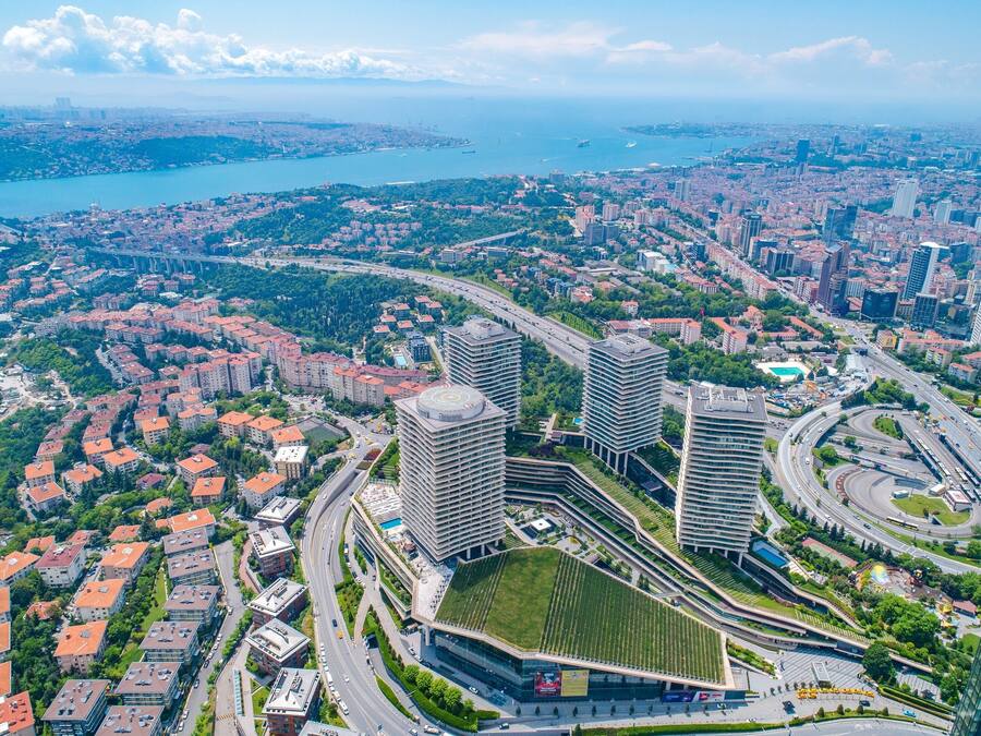 An aerial view of a cityscape with modern buildings, a large roundabout, and a body of water in the background.