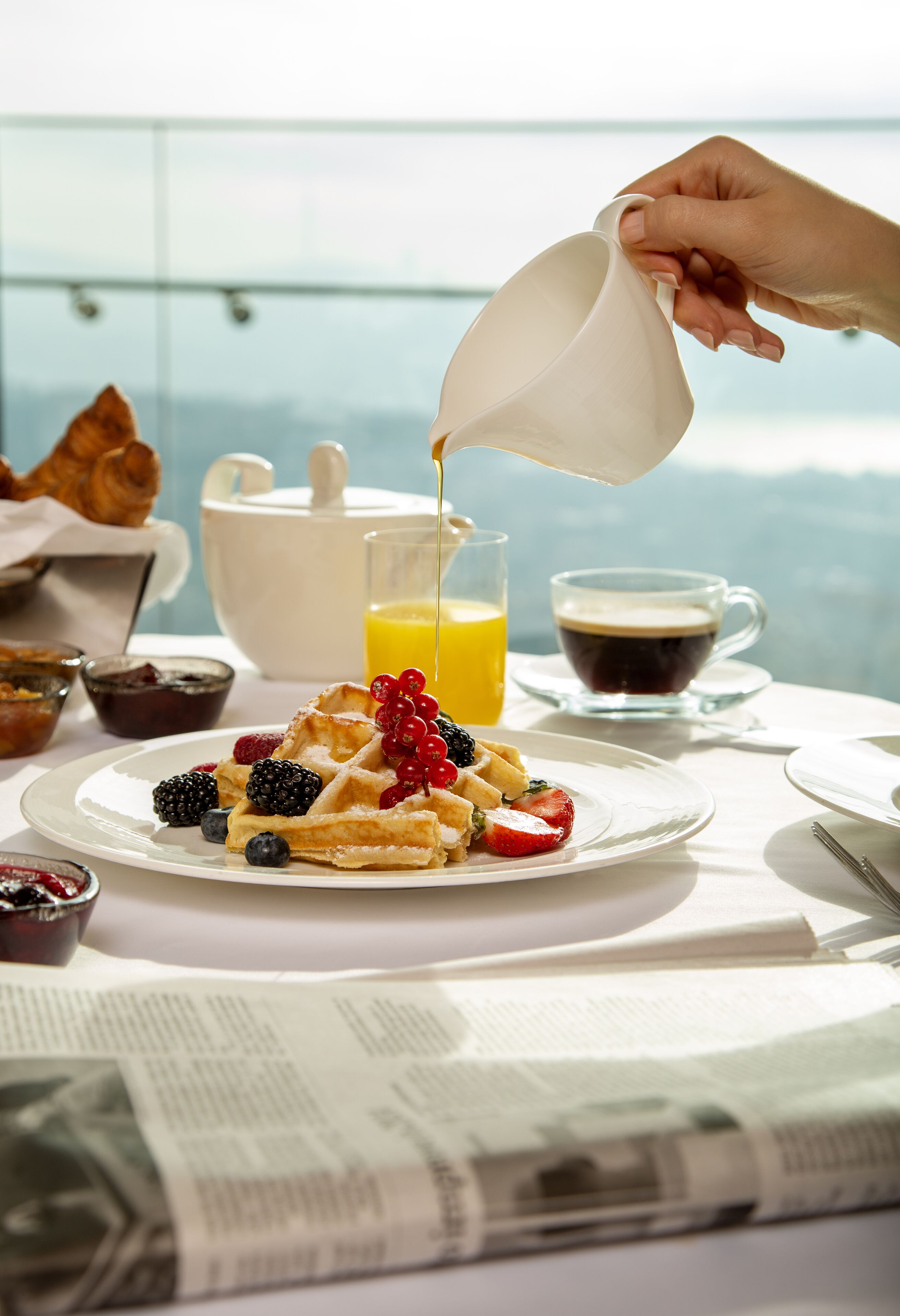 Desayuno con gofres, bayas y un recipiente sirviendo almíbar.